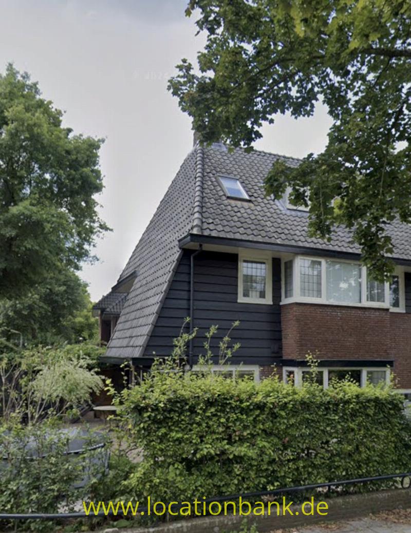 Altes Haus aus dem 30 zigger Jahren mit einem Ziegeldach, dunkler Holzverkleidung, einer Backsteinfassade und weißen Fensterrahmen.