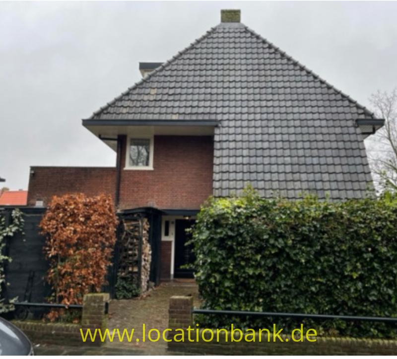 Freistehendes Haus mit großem grauem Ziegeldach, Backsteinfassade, Vorgarten und überdachtem Eingang.