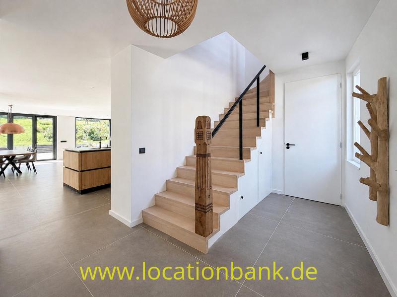 Holztreppe mit schwarzem Handlauf in einem hellen Flur neben einer weißen Tür.