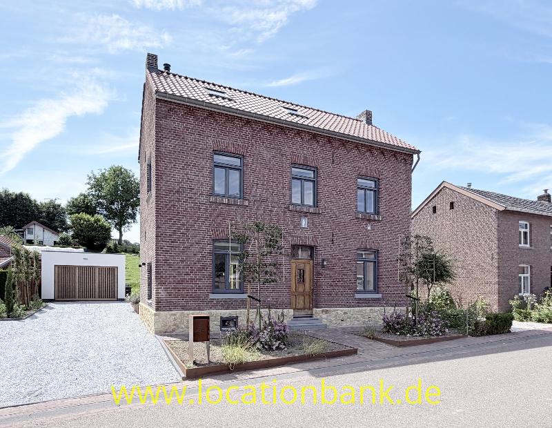 Vorseite Zweistöckiges rotes Ziegelhaus mit Satteldach, hölzerner Eingangstür und freistehender Garage.