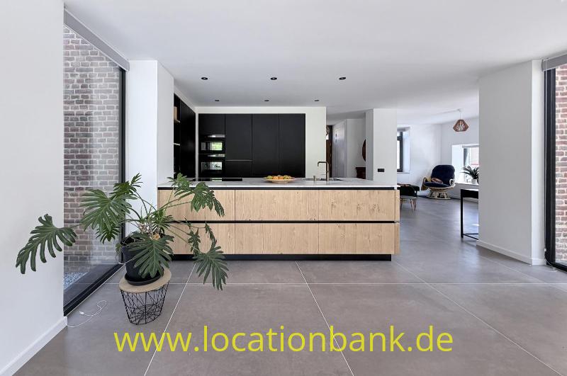 Offene Küche mit einer großen Kücheninsel aus Holz, schwarzen Schränken, einer Zimmerpflanze und einer Backsteinwand.