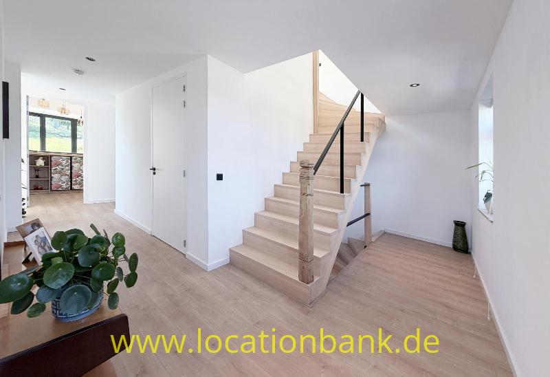 Holztreppe mit schwarzem Handlauf in einem hellen Flur mit Holzboden und Zimmerpflanzen.