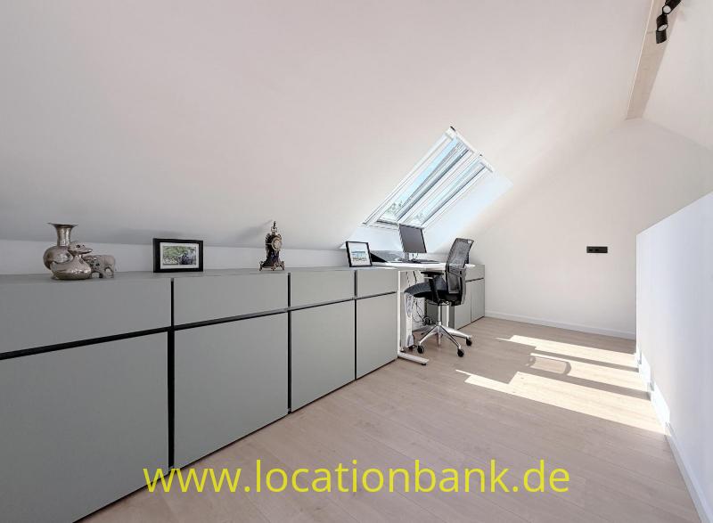 Lange niedrige Schrankwand in einem hellen Dachraum mit einem Dachfenster, Schreibtisch und Bürostuhl.