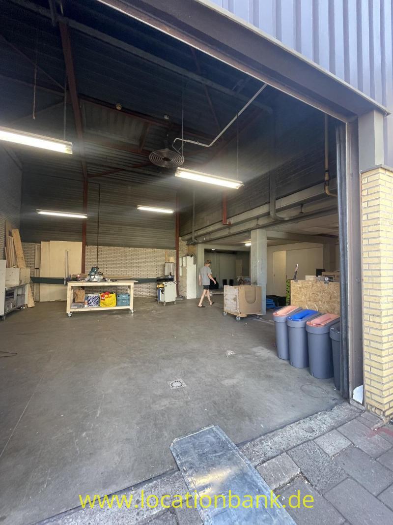 Eine offene Halle mit einer Metallkonstruktion am Dach, Werkbänken, Abfallbehältern und einer Person am Eingang.
