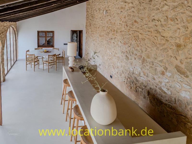 Lange Theke mit Barhockern und weißen Vasen an einer rauen Steinwand.
