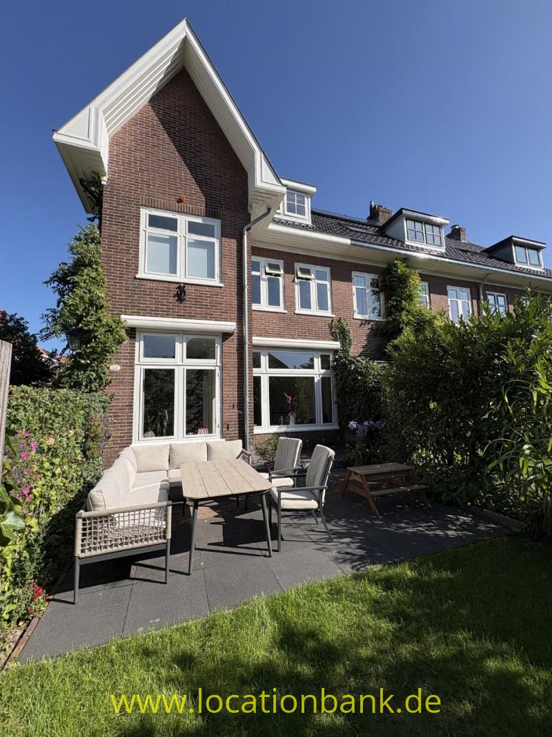 Backsteinhaus mit Giebelfront, weißen Fensterrahmen und einer Terrasse mit Gartenmöbeln.