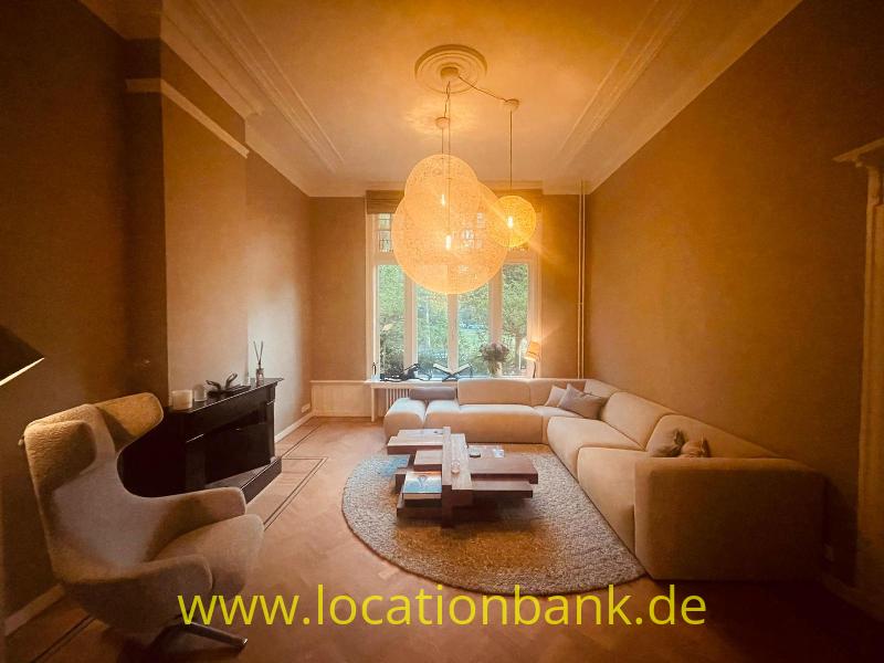 Wohnzimmer mit einem beigefarbenen Ecksofa, Pendelleuchten, rundem Teppich und hohen Fenstern.