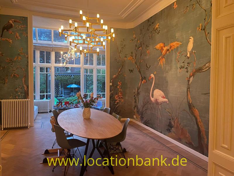 Esszimmer mit einem ovalen Holztisch, einem Kronleuchter und einer Tapete mit Vogelmotiven.