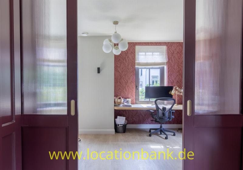 Offene dunkelrote Doppeltüren geben den Blick auf einen Raum mit Schreibtisch, Monitor und Bürostuhl frei.