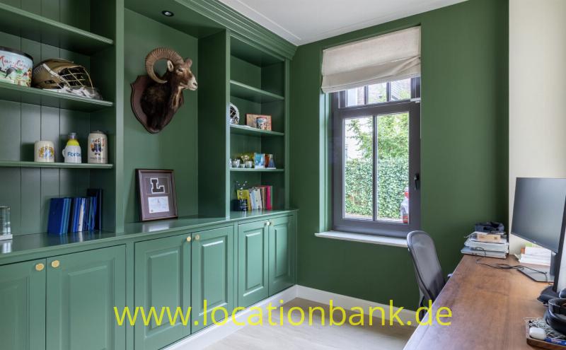 Grüne Einbauschränke und Bücherregale umrahmen ein Fenster neben einem Holzschreibtisch und einem aufgehängten Widderkopf.