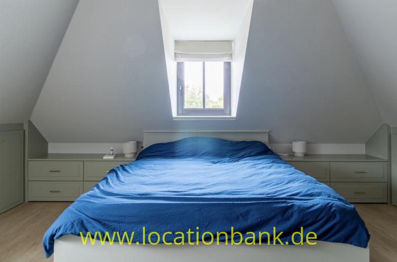 Blaues gemachtes Bett unter einem Dachfenster mit Einbauschränken und Nachttischen auf beiden Seiten.