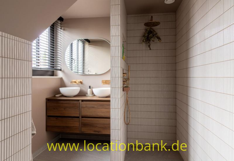Badezimmer mit zwei Waschbecken, hölzernem Waschtischunterschrank, großem Spiegel und einer gefliesten Dusche mit Regenduschkopf.