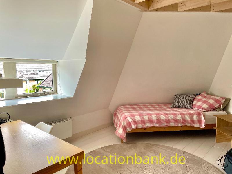 Ein Einzelbett mit rot-weiß karierter Bettwäsche steht unter einer Dachschräge neben einem Schreibtisch.