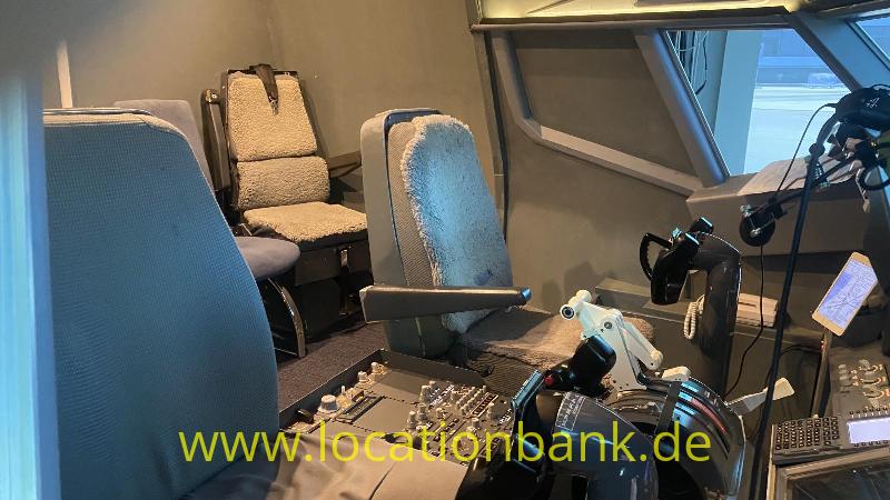 Cockpit mit mehreren Sitzen, Bedienpulten, Steuerhörnern und großen Fenstern an der Vorderseite.