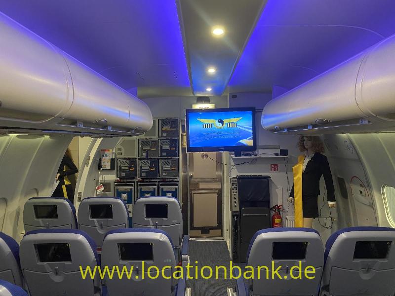 Flugzeugkabine mit Reihen von Passagiersitzen, einem Bildschirm und blauer Deckenbeleuchtung.