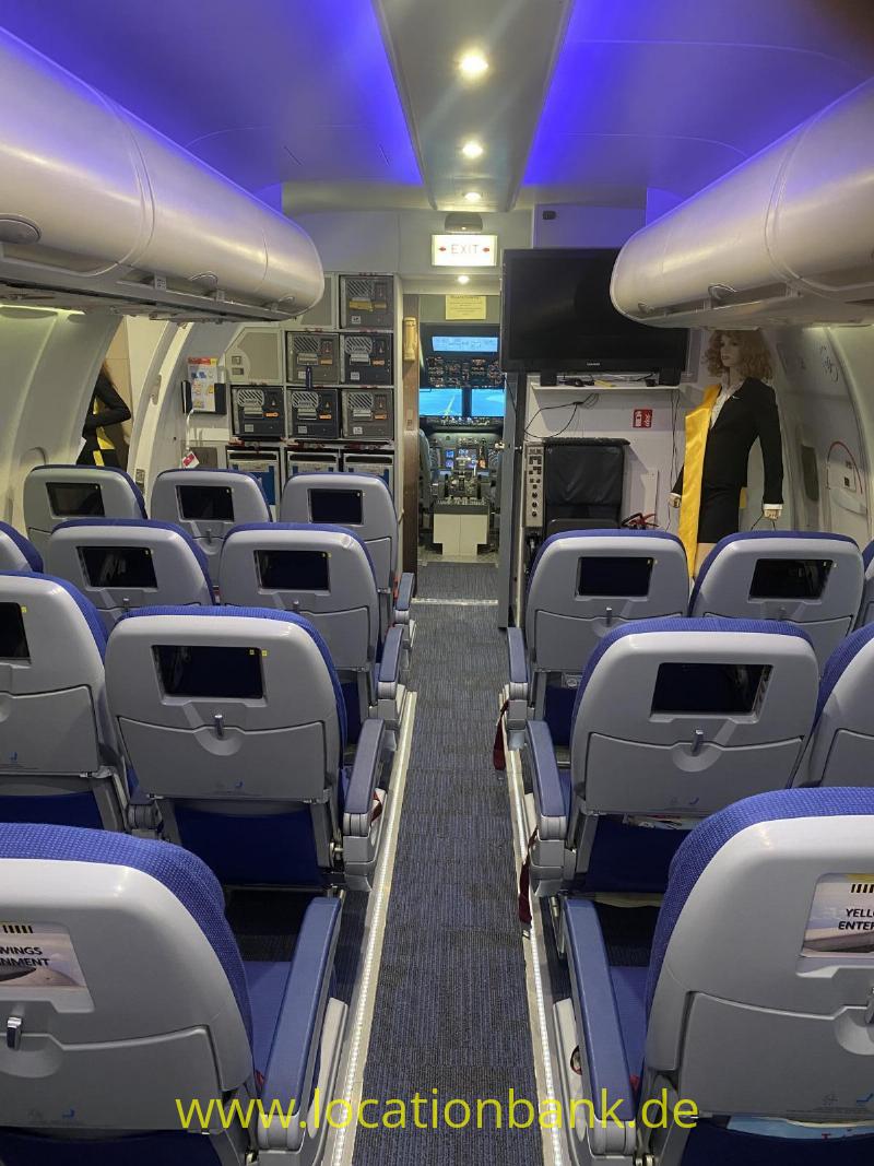 Flugzeugkabine mit Reihen blauer Passagiersitze, einem Mittelgang, Gepäckfächern und blauer Deckenbeleuchtung.