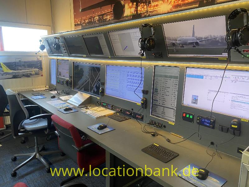 Ein langer Arbeitsplatz mit mehreren Computerbildschirmen, aufgehängten Headsets und Bürostühlen.