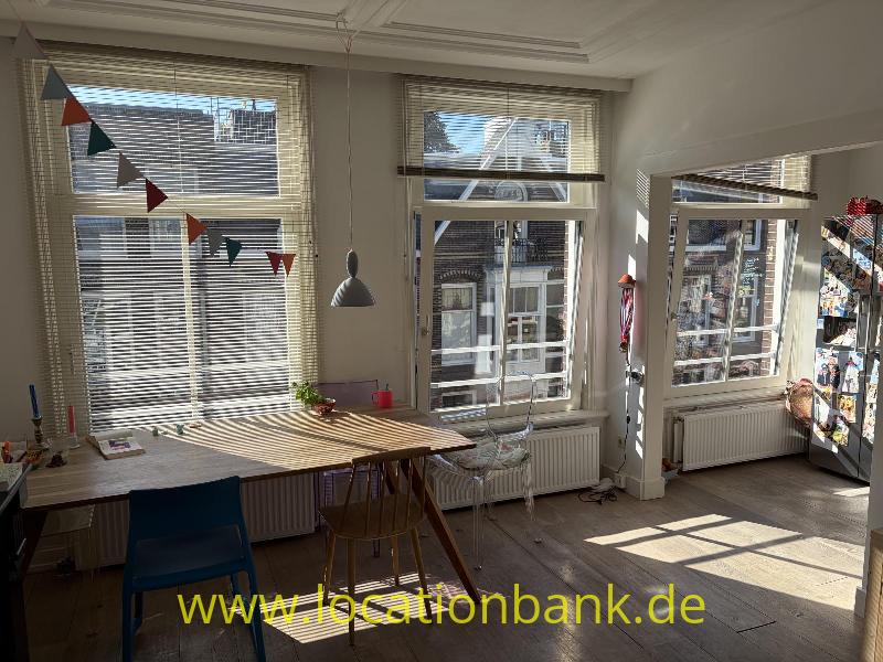 Heller Raum mit einem Holztisch, Stühlen, großen Fenstern und einer Wimpelkette.