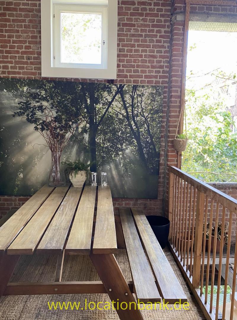 Ein hölzerner Picknicktisch mit Bänken steht vor einer Backsteinwand neben einem Holzgeländer.