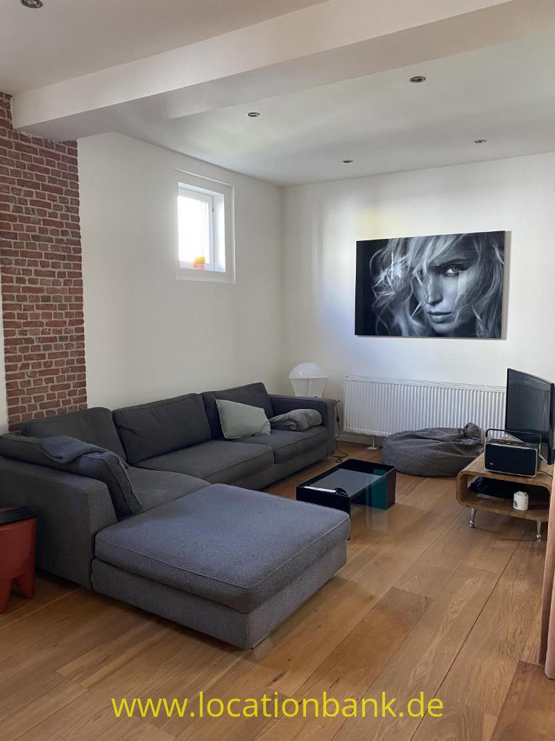 Graues Ecksofa mit Chaiselongue in einem Wohnzimmer mit Holzboden, Backsteinwand und Schwarz-Weiß-Porträt.