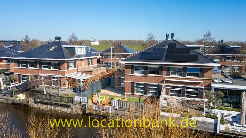 Reihe von Backsteinhäusern mit Solarmodulen an einem schmalen Wasserlauf und Holzstegen.