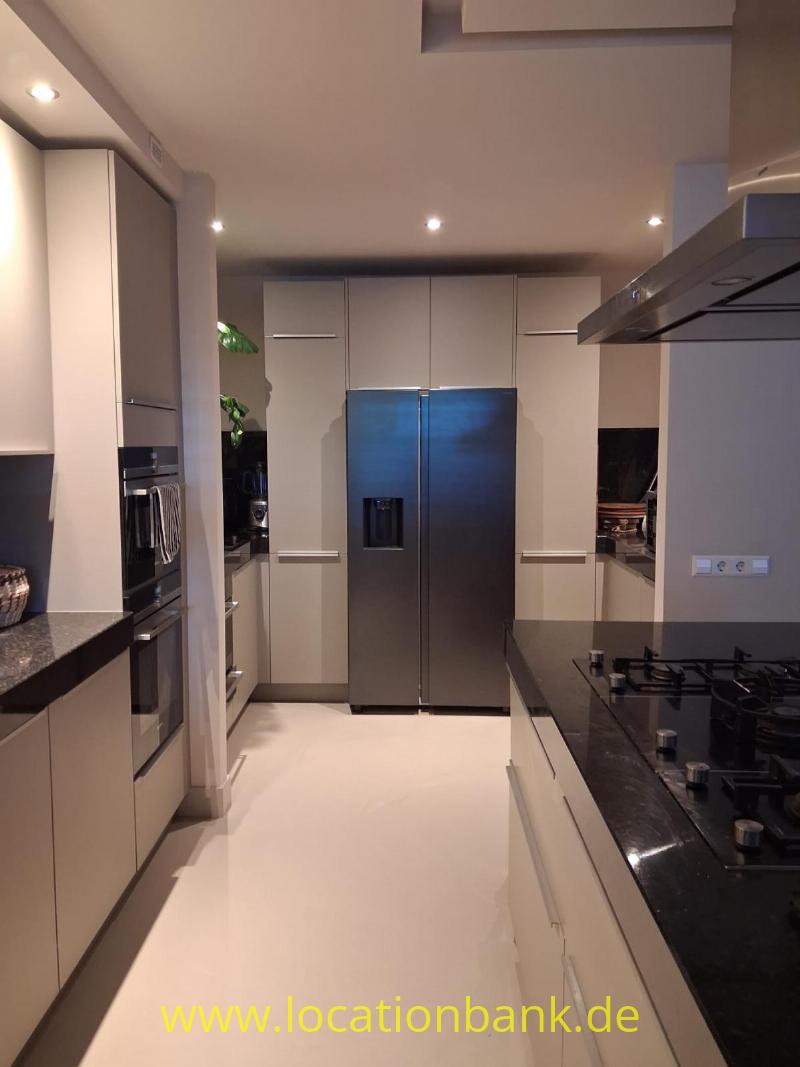 Moderne Küche mit einem zentral platzierten Kühlschrank mit zwei Türen, weißen Schränken und schwarzen Arbeitsplatten.