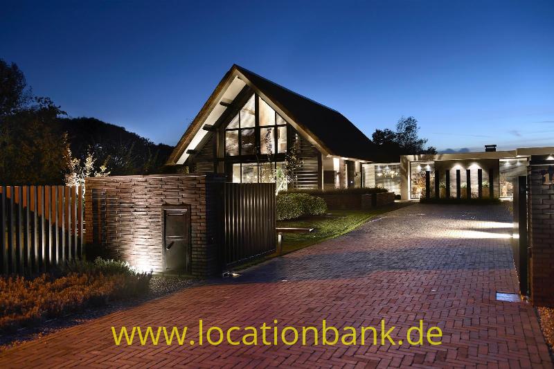 Haus mit steilem Satteldach, verglaster Fassade, Holztor und breiter Zufahrt mit Ziegelpflaster.