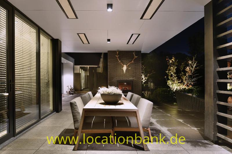 Esstisch mit Stühlen neben Glastüren und einer gefliesten Terrasse mit Pflanzen.