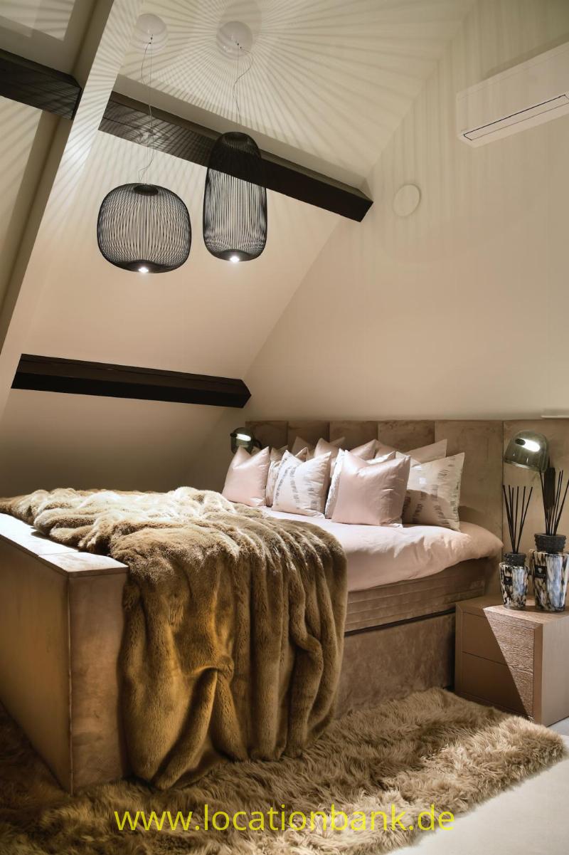 Bett mit rosa- und weißen Kissen, einer braunen Decke und Pendelleuchten unter einer schrägen Decke.