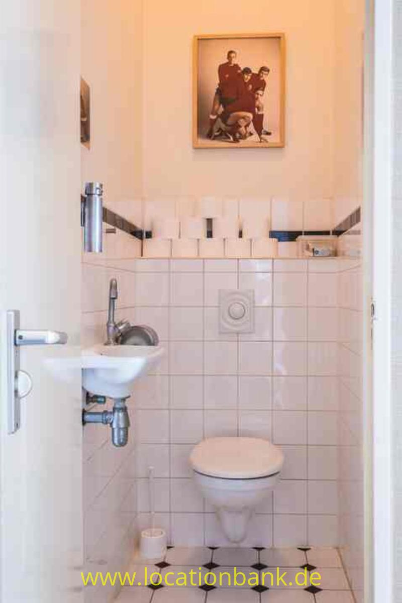 Ein kleines gefliestes WC mit einem Waschbecken, einem wandhängenden WC und einem gerahmten Bild an der Wand.