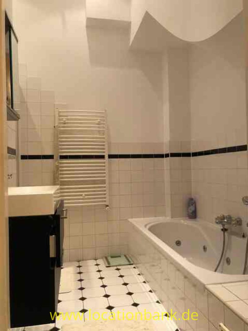 Ein gefliestes Badezimmer mit einer Badewanne, einem weißen Handtuchheizkörper und einem schwarzen Waschtischunterschrank.