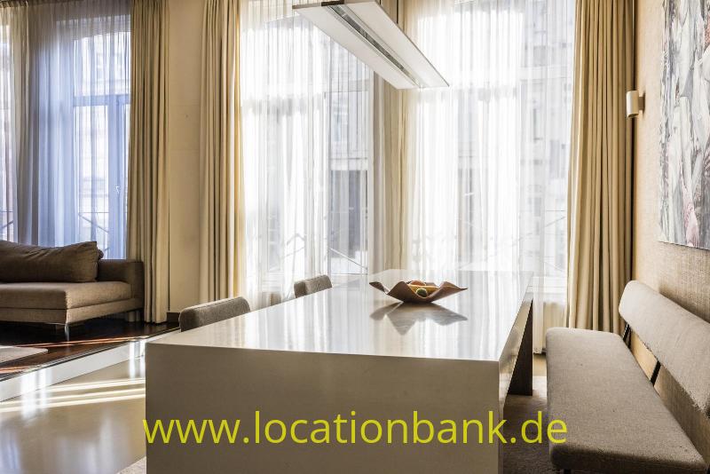 Innenraum mit einem langen weißen Tisch, Stühlen, Sofas und hohen Fenstern mit Vorhängen.