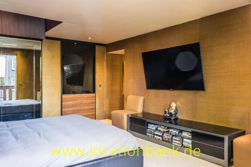 Schlafzimmer mit einem großen Bett, einem an der Wand montierten Fernseher und einem niedrigen dunklen Sideboard.