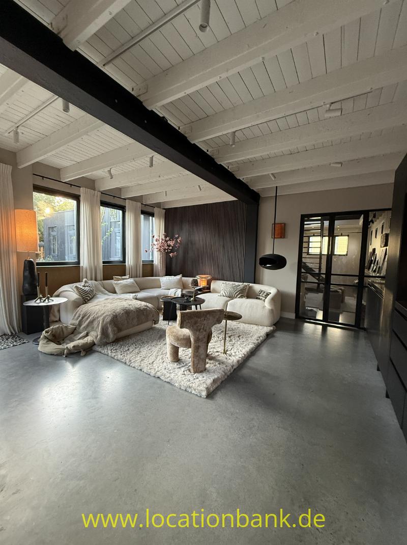 Wohnzimmer mit sichtbaren weißen Deckenbalken, Sofas, einem großen Teppich und schwarz gerahmten Glastüren.
