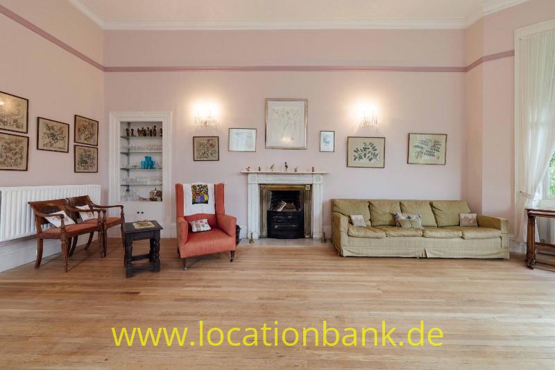 Wohnzimmer mit einem Kamin, einem langen Sofa, einem Sessel und gerahmten Bildern an den Wänden.