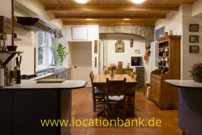 Offene Küche, Holztisch, Terrakottafliesen und sichtbaren Holzbalken an der Decke.
