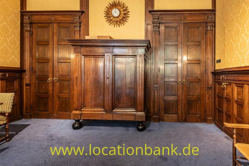 Dunkler Holzschrank zwischen zwei Kassettentüren, darüber eine sonnenförmige Uhr.
