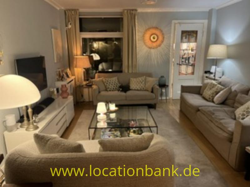 Wohnzimmer mit zwei beigefarbenen Sofas, einem gläsernen Couchtisch, Tischlampen und einem runden Wandschmuck.