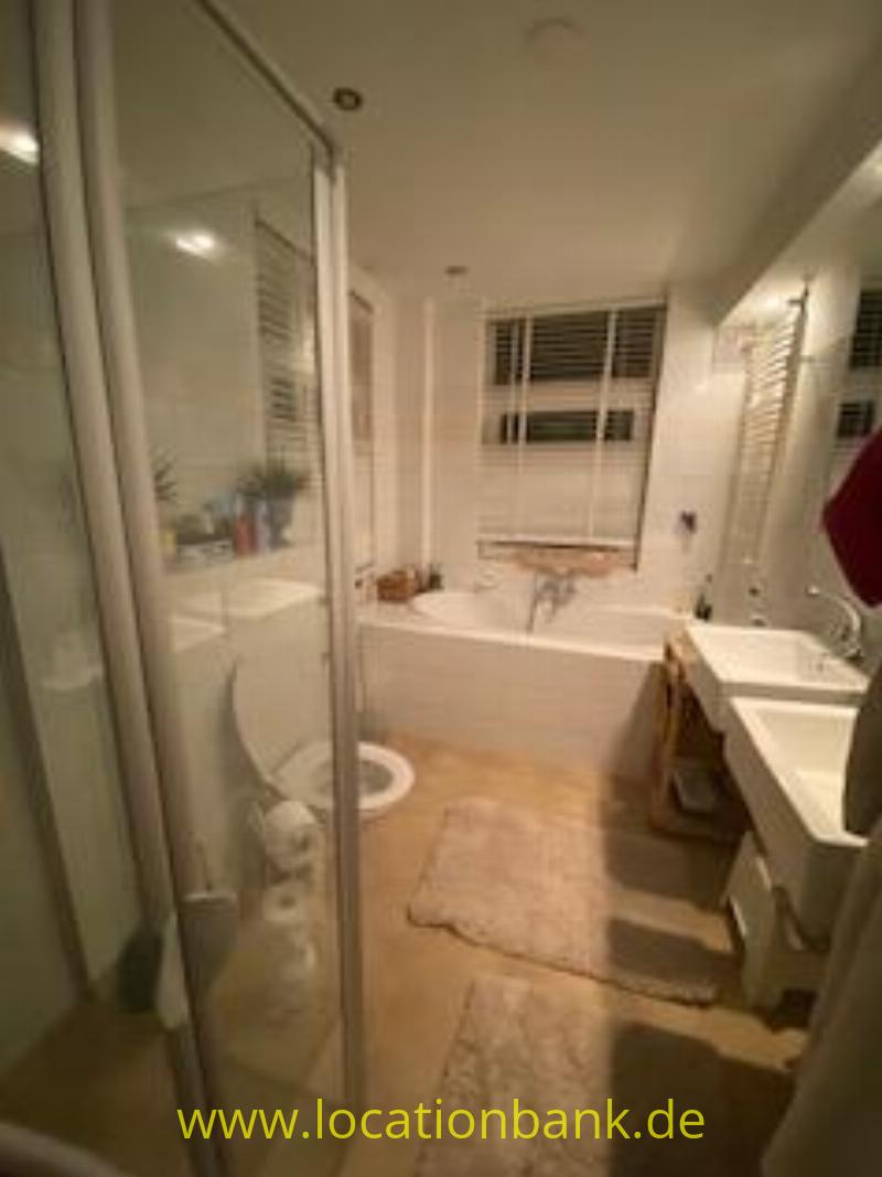 Badezimmer mit einer Badewanne unter dem Fenster, einer gläsernen Duschkabine, einer Toilette und einem Waschbecken.