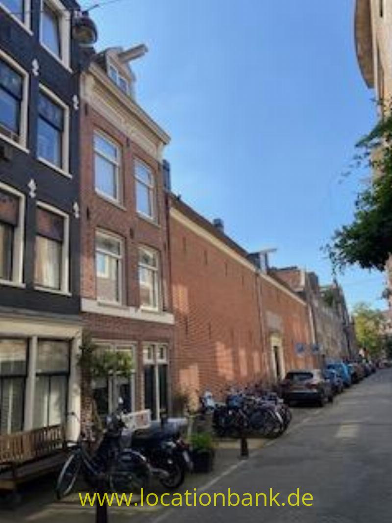 Backsteinfassaden säumen eine schmale Straße mit abgestellten Fahrrädern und Bäumen unter einem klaren blauen Himmel.