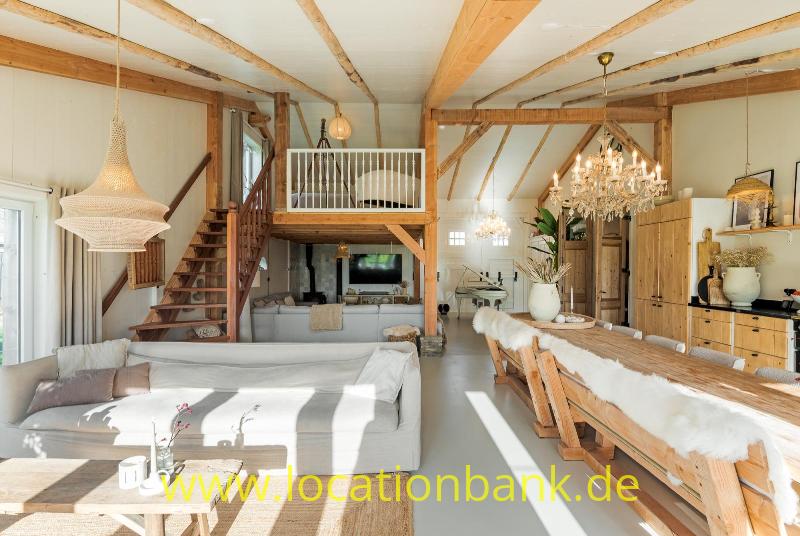 Grosse Wohnzimmer mit sichtbaren Holzbalken, einer Treppe zu einer Galerie und einem langen Esstisch.