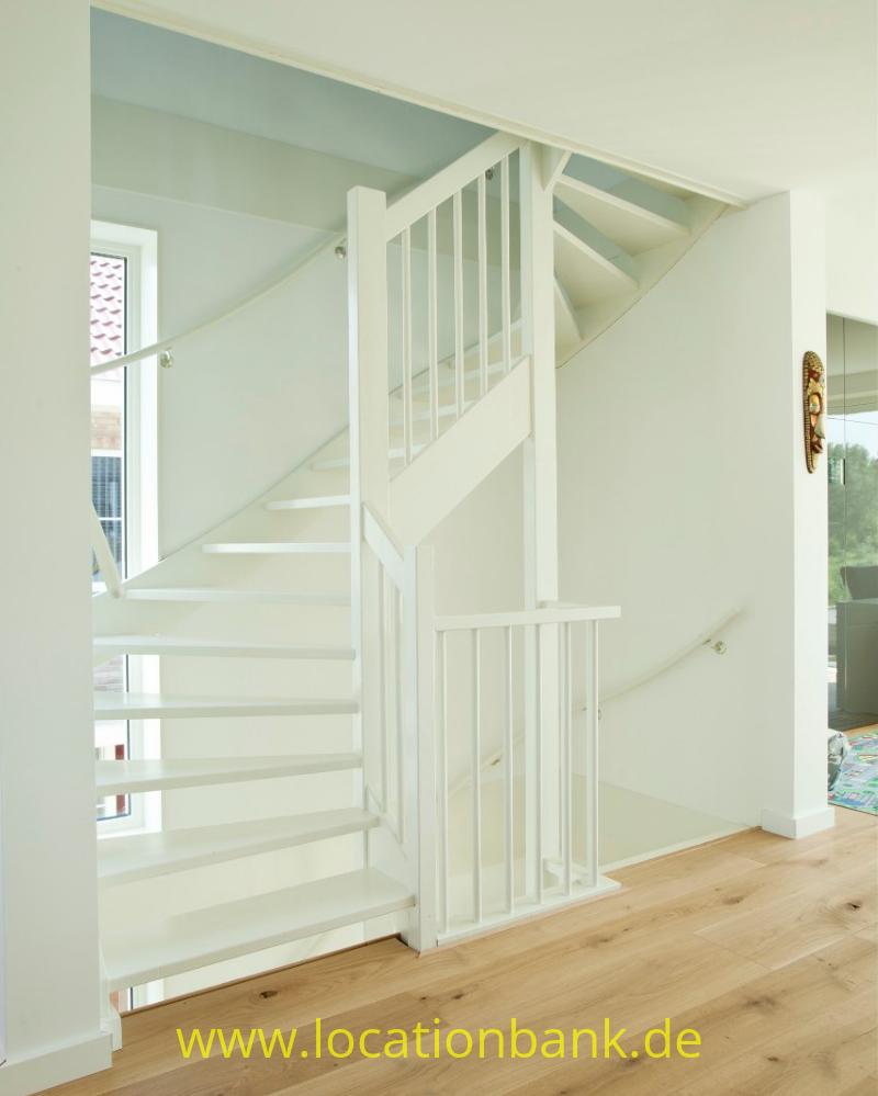 Weiße Treppe mit offenen Stufen und senkrechten Geländerstäben führt von einem Holzboden nach oben.