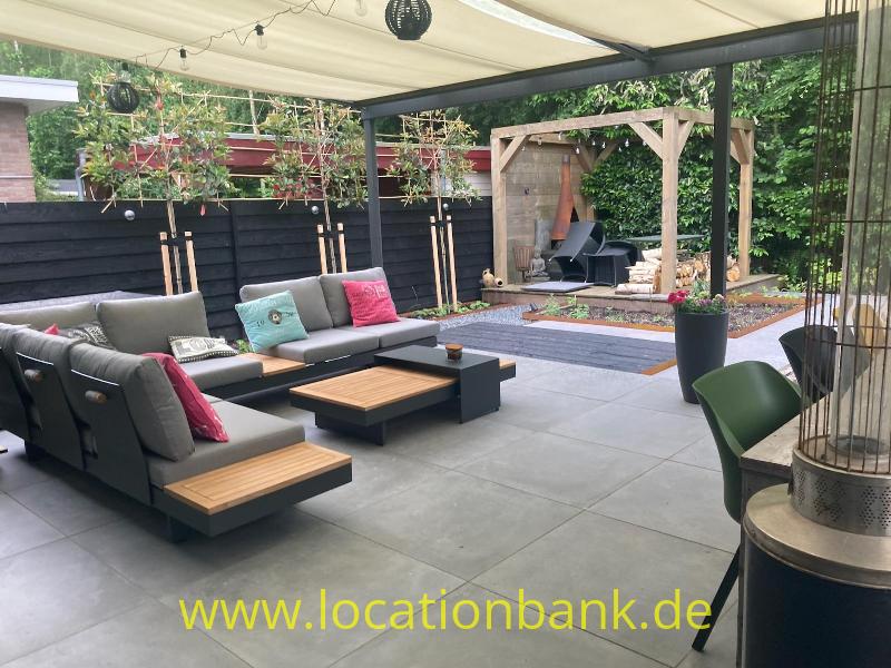 Überdachte Terrasse mit modularen Loungesofas, niedrigen Holztischen, Pflanzgefäßen und einer Holzpergola.