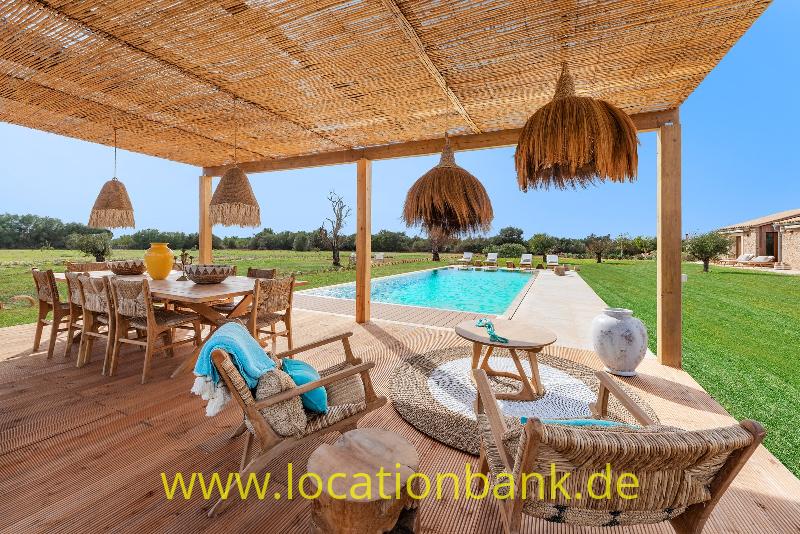 Überdachte Terrasse mit geflochtenen Hängelampen, Holztisch und Liegestühlen neben einem rechteckigen Swimmingpool.