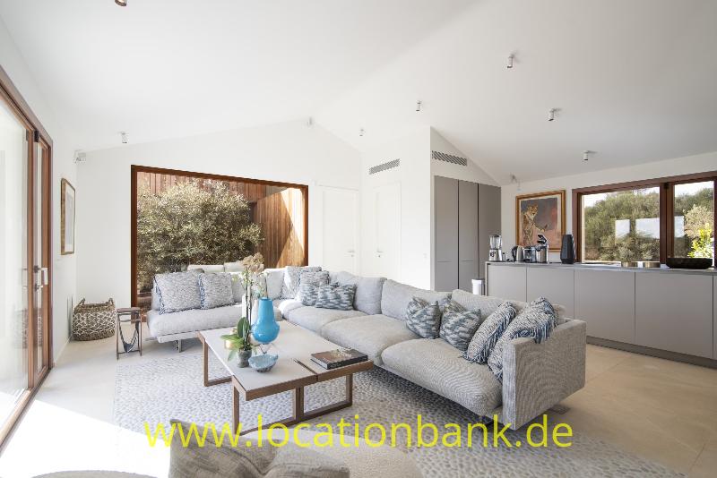 Geräumiges Wohnzimmer mit einem grauen Ecksofa, einem niedrigen Couchtisch und großen Fenstern neben einer offenen Küche.