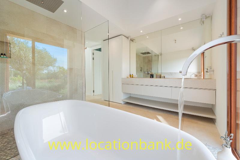 Freistehende weiße Badewanne im Vordergrund eines modernen Badezimmers mit Doppelwaschbecken und gläserner Duschwand.