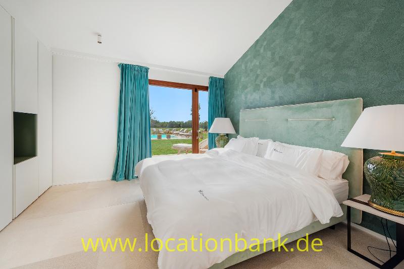 Schlafzimmer mit einem bezogenen Doppelbett, einer strukturierten grünen Wand und türkisfarbenen Vorhängen am Fenster.