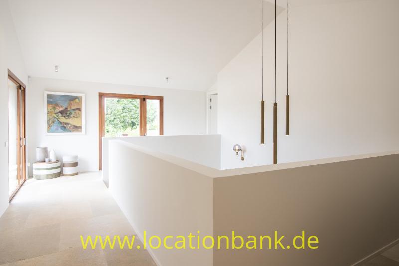 Innenraum mit weißen Wänden, einer niedrigen Trennwand, drei Pendelleuchten und hölzernen Fensterrahmen.