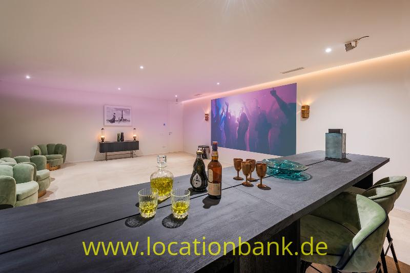 Dunkler Esstisch mit Gläsern und Flaschen, umgeben von Stühlen und einem farbenfrohen Kunstwerk an der Wand.