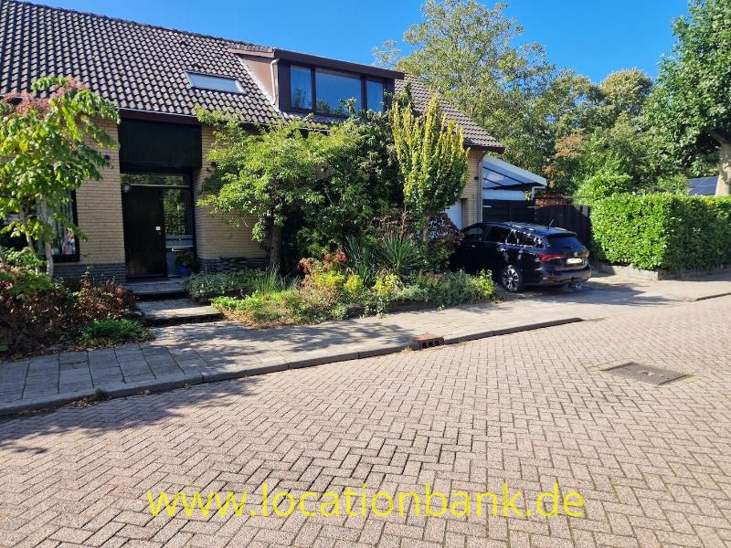 Backsteinhaus mit angebauter Garage, Vorgarten und schwarzem Auto an einer gepflasterten Straße.